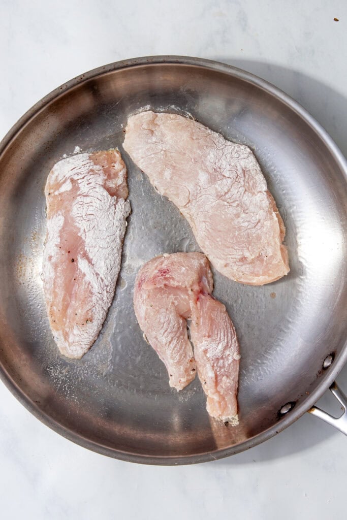 Floured chicken pieces placed into a hot stainless steel pan.