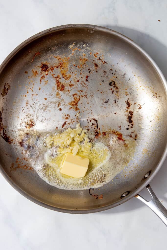 Butter melting with minced garlic in the same pan, showing browned bits stuck to the bottom.