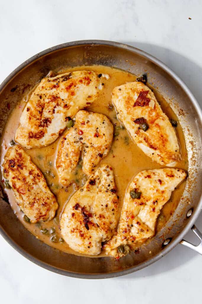 Seared chicken simmering in the thickened sauce with capers for an easy chicken piccata recipe.