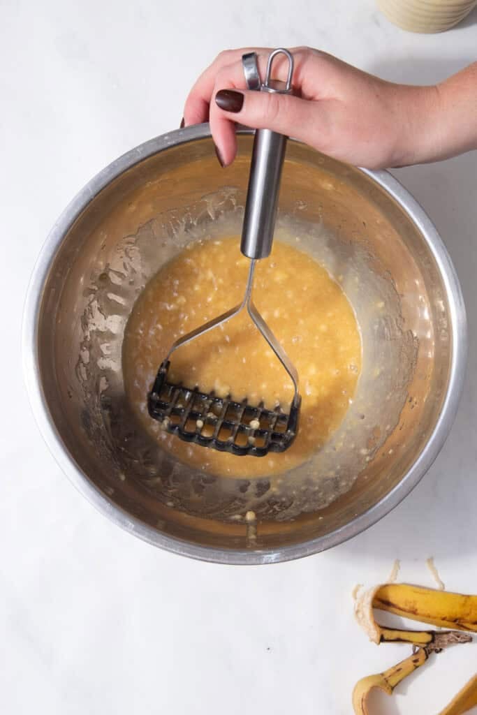 Mashing ripe bananas into the butter and sugar mixture for the chocolate protein muffins.
