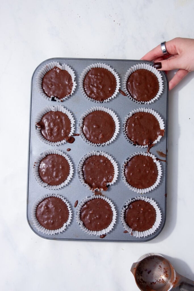 Dividing the chocolate protein muffin batter into paper-lined muffin tins, ready to bake.