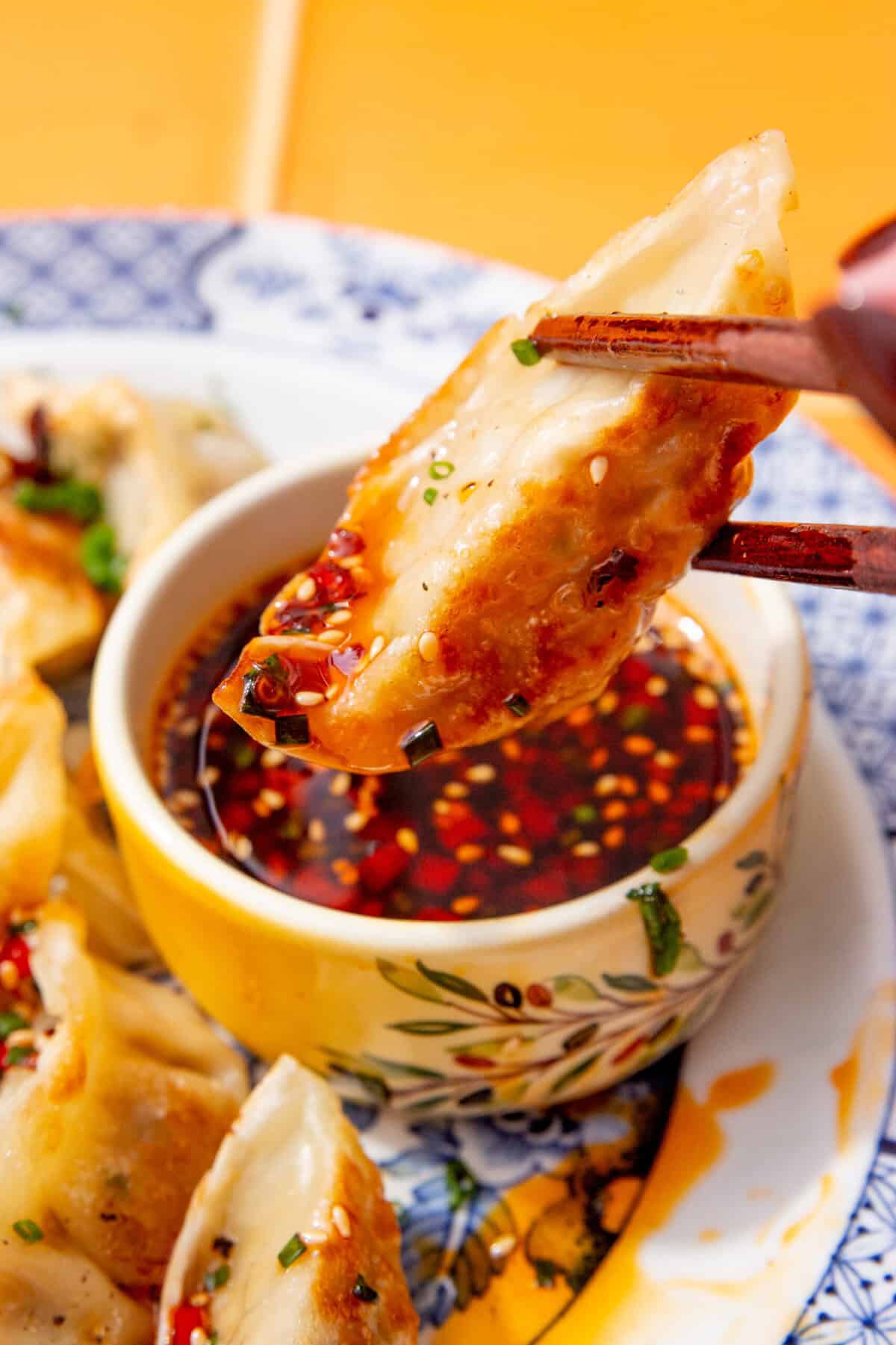 Crispy gyoza dumpling being dipped into a bowl of gyoza dipping sauce with sesame seeds and chilli oil.