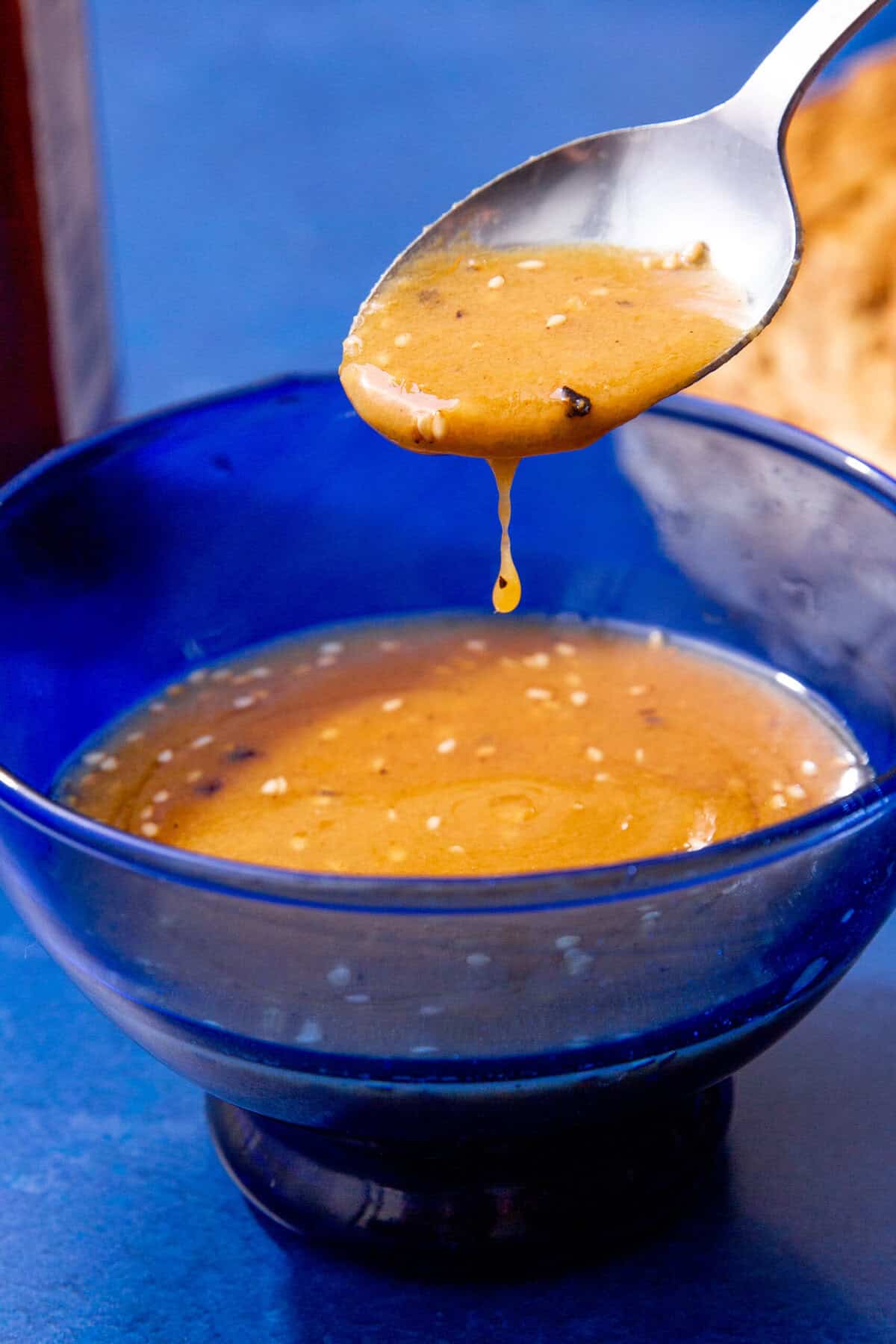 Spoon drizzling creamy miso dressing from a blue bowl.