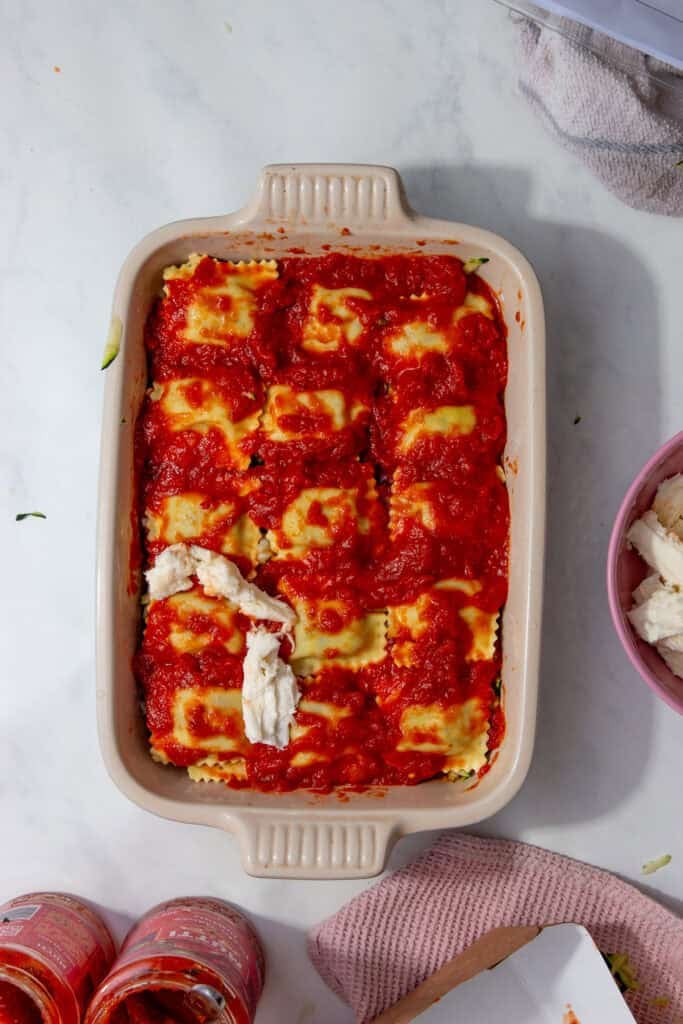 A baking dish with the ravioli arranged over marinara sauce with mozzarella on top.