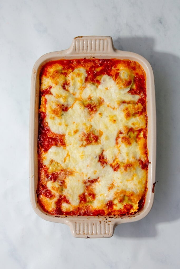 Fully baked ravioli casserole in a beige dish with melted, golden cheese on top.