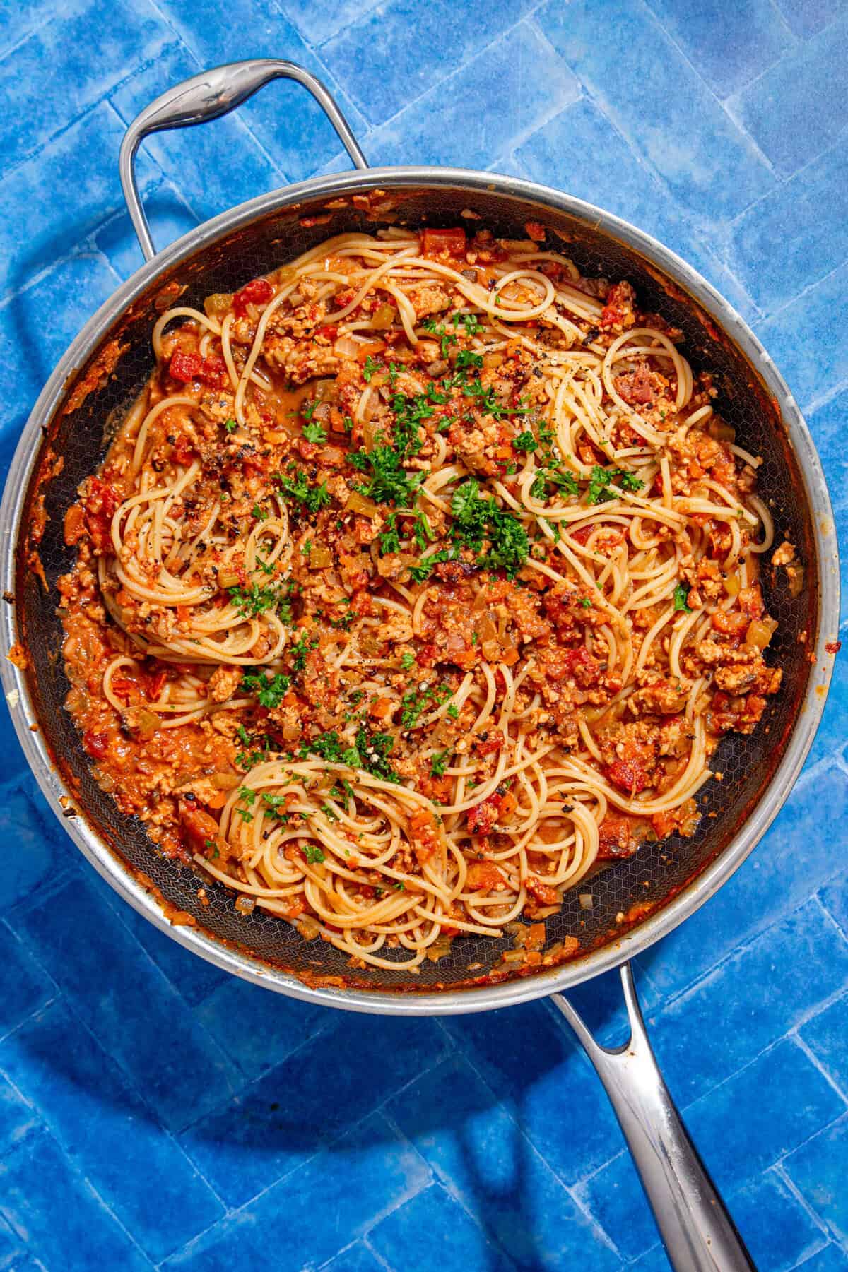 Cooked spaghetti topped with a chicken bolognese sauce, garnished with chopped parsley.