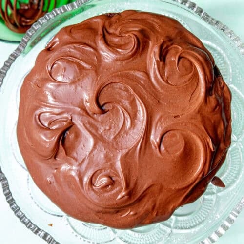 Chocolate cream cheese frosting swirled smoothly over a chocolate cake on a glass stand.