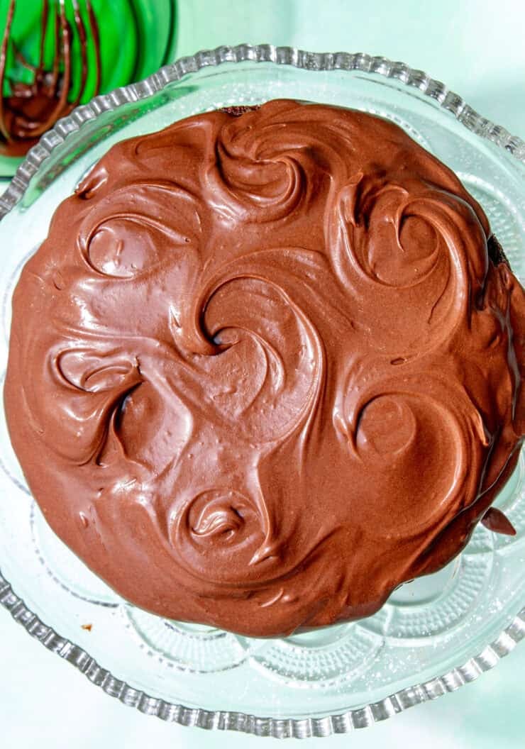 Chocolate cream cheese frosting swirled smoothly over a chocolate cake on a glass stand.
