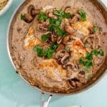 A skillet filled with cream of mushroom chicken breasts in a creamy sauce, garnished with fresh parsley. Nearby are bowls of cooked spaghetti and green peas.