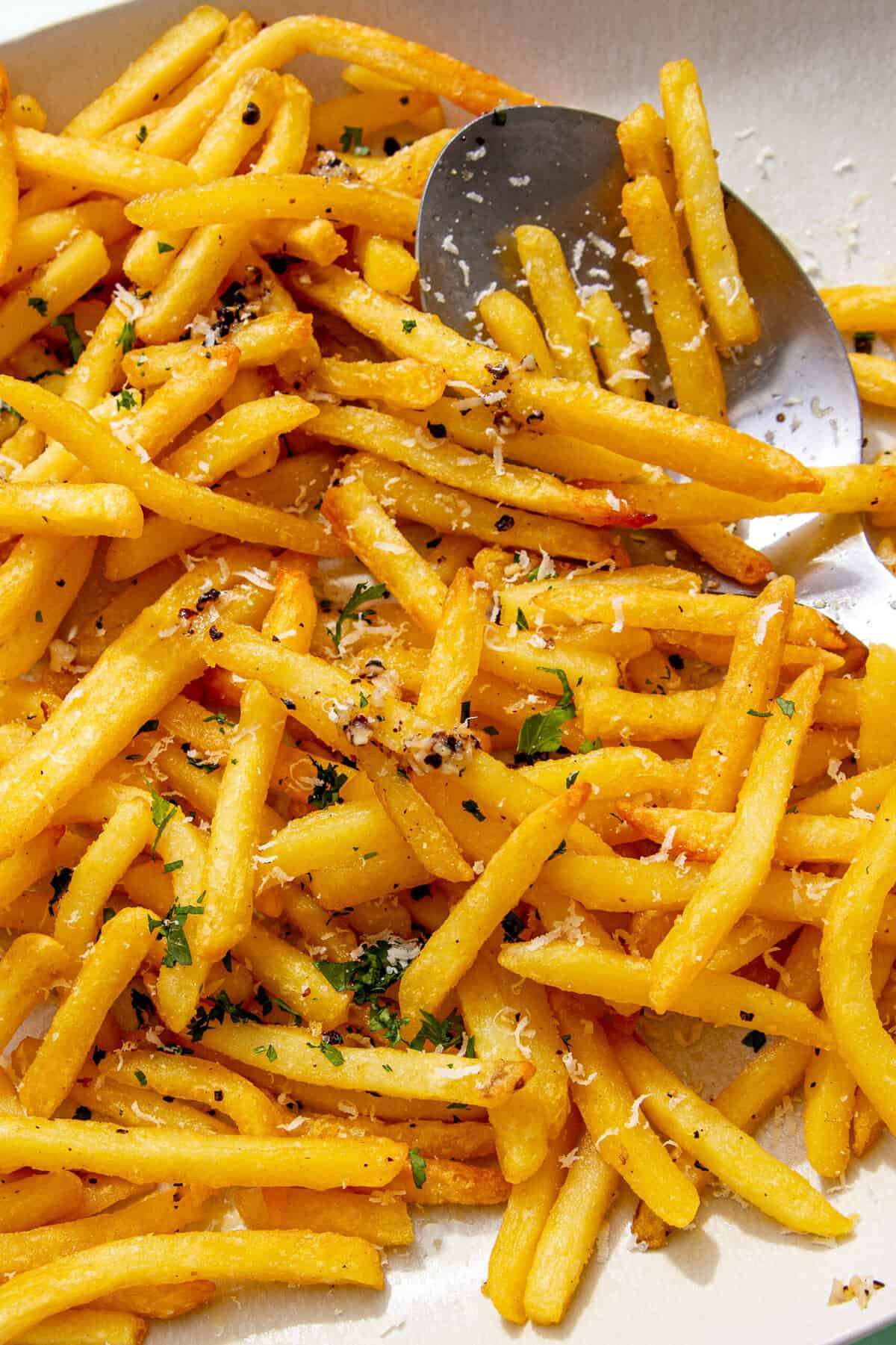 Close-up of golden garlic fries sprinkled with grated parmesan, chopped parsley, and cracked black pepper, showing their crispy texture.