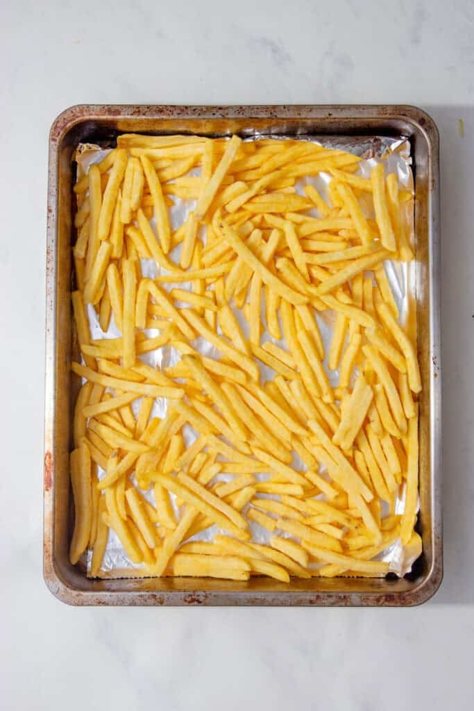 Frozen fries spread evenly on a foil-lined baking tray.
