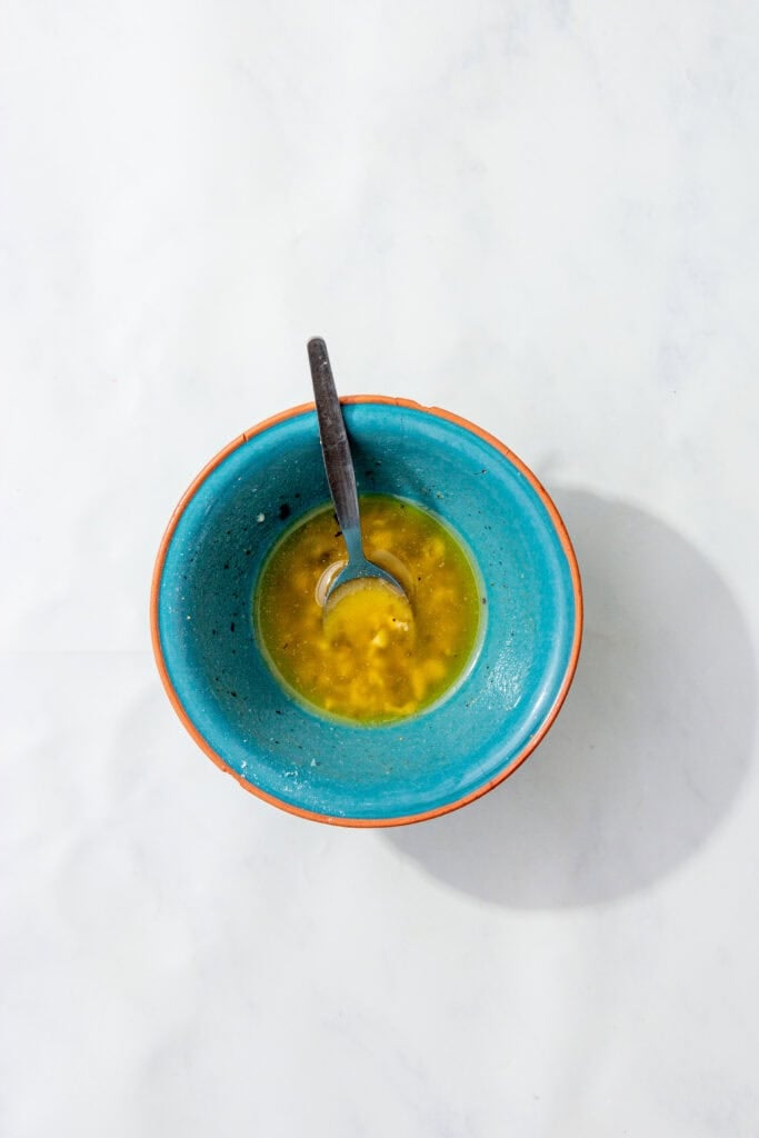 Melted garlic butter mixture in a blue bowl, with a spoon resting inside.