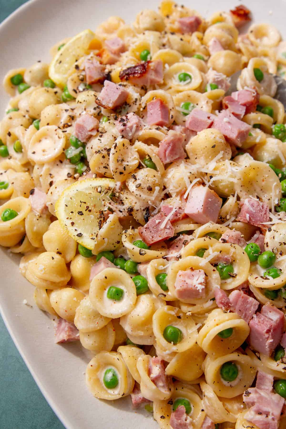 Close-up of creamy leftover ham pasta with peas, lemon slices, and black pepper on top.