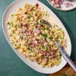 Large serving platter of creamy leftover ham pasta with peas, lemon slices, and Parmesan, ready to serve with chopped chives on the side.
