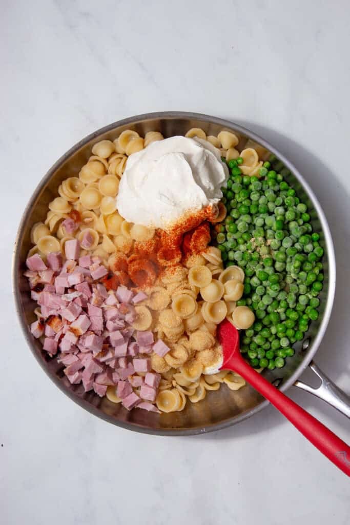 Drained pasta returning to the pan with a red spatula ready to stir.