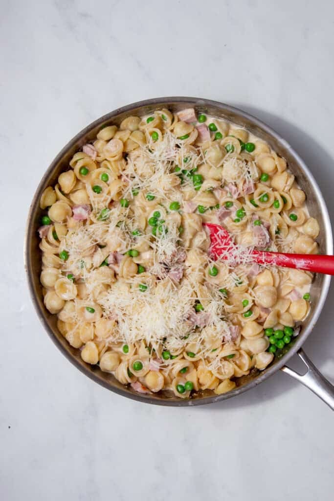 Creamy ham and pea pasta in a pan with cheese melting into the sauce.