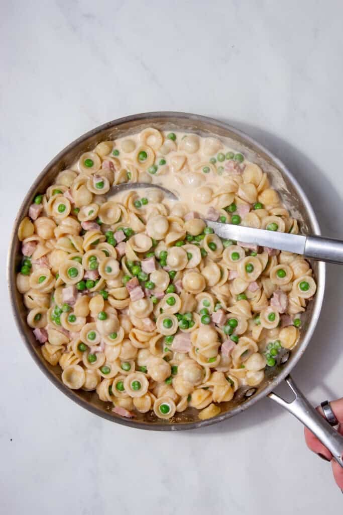 Finished creamy ham and pea pasta topped with cheese and peas in a stainless-steel pan, ready to serve.
