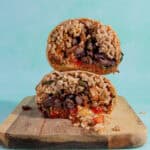 Two halves of a burrito, filled with rice, black beans, vegetables, and sauce, are stacked on a wooden cutting board against a light turquoise background—perfect for learning how to reheat a burrito while keeping it fresh and delicious.