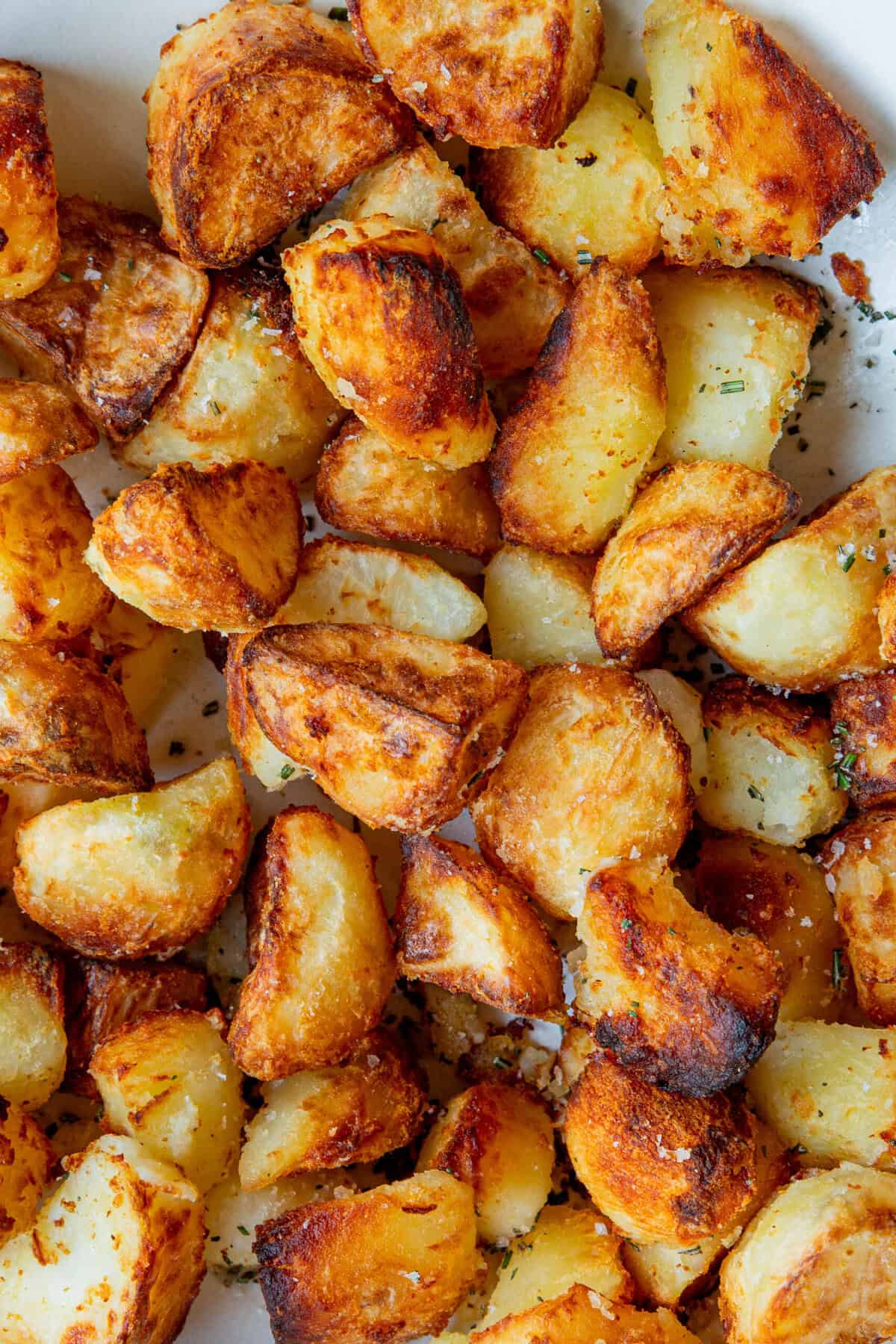 Golden, crispy roasted potato chunks with a sprinkle of herbs and salt, piled closely together to show their crunchy, browned exteriors and fluffy insides.