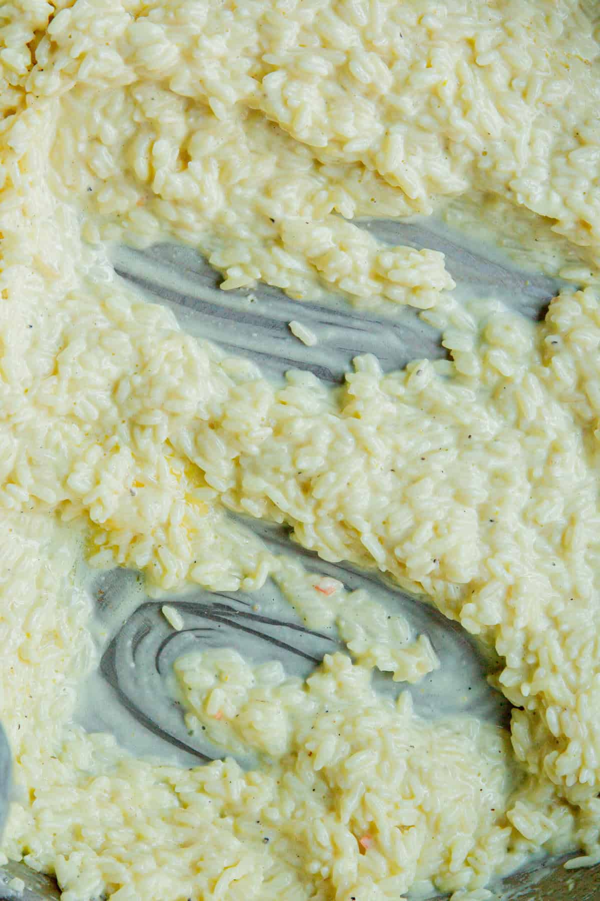 Close-up of creamy risotto being stirred, revealing a thick, yellowish Creamy Rice mixture with visible streaks and a smooth, glossy texture.