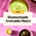 Flat lay of ingredients for creamy Avocado Mayo on a pink background: halved avocados, a bowl of avocado mayo, mustard, oil, an egg, and lemon. Text overlay: Easy Homemade Avocado Mayo.