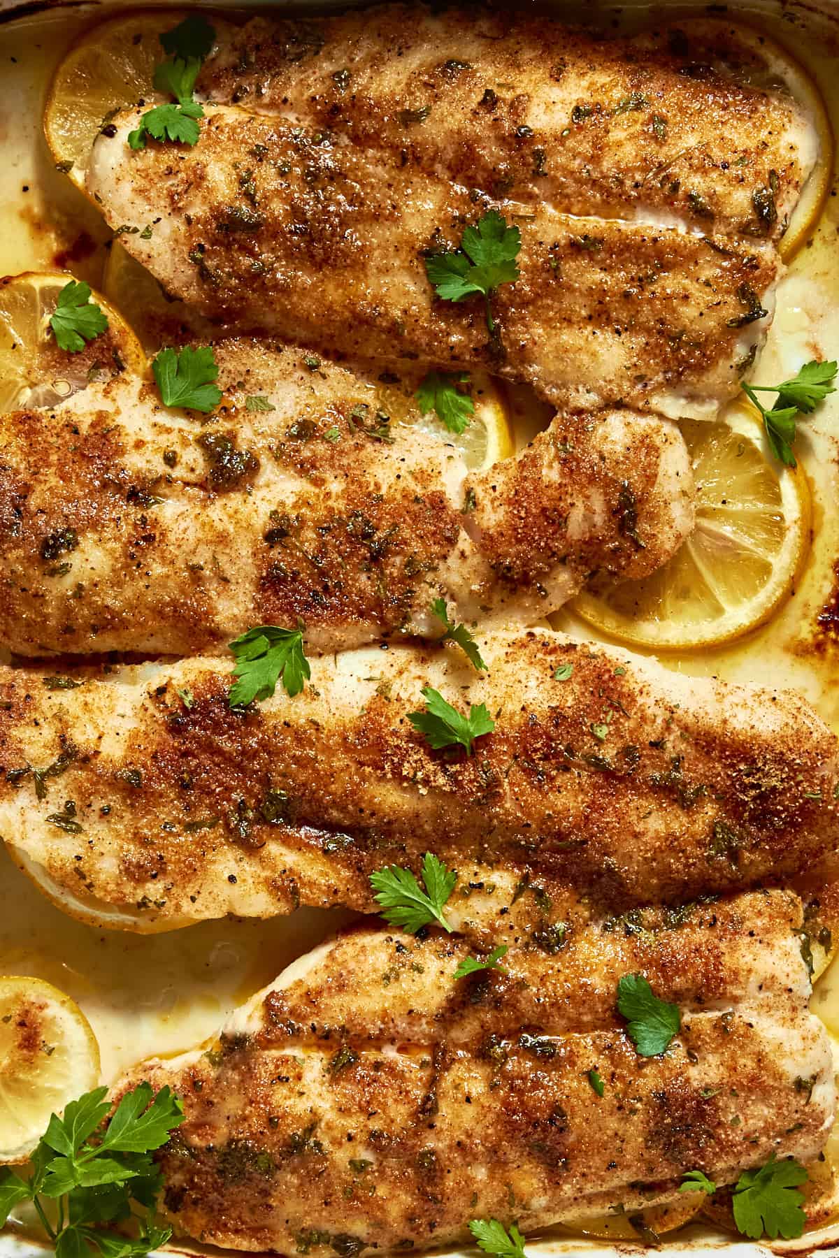 Baked white fish fillets seasoned with spices, served atop lemon slices and garnished with fresh parsley and roasted corn for added flavor and texture.
