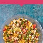 A bowl filled with Mexican chicken salad, featuring roasted corn, bacon, chopped vegetables, lime wedges, and herbs on a blue surface. A pink banner above reads “Perfect for Meal Prep – Mexican Chicken Salad with Roasted Corn and Bacon.”.