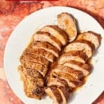 Sliced slow cooker pork loin served on a white plate, with herbs nearby and a slow cooker partially visible; text reads Pork Loin Crock Pot Recipe and Easy Fuss-Free Family Dinner.