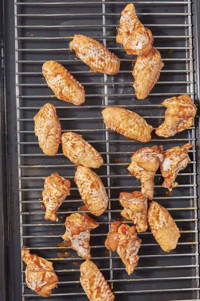Raw soy chicken wings coated in barbecue sauce are arranged on a metal rack above a dark baking tray, ready to be cooked.