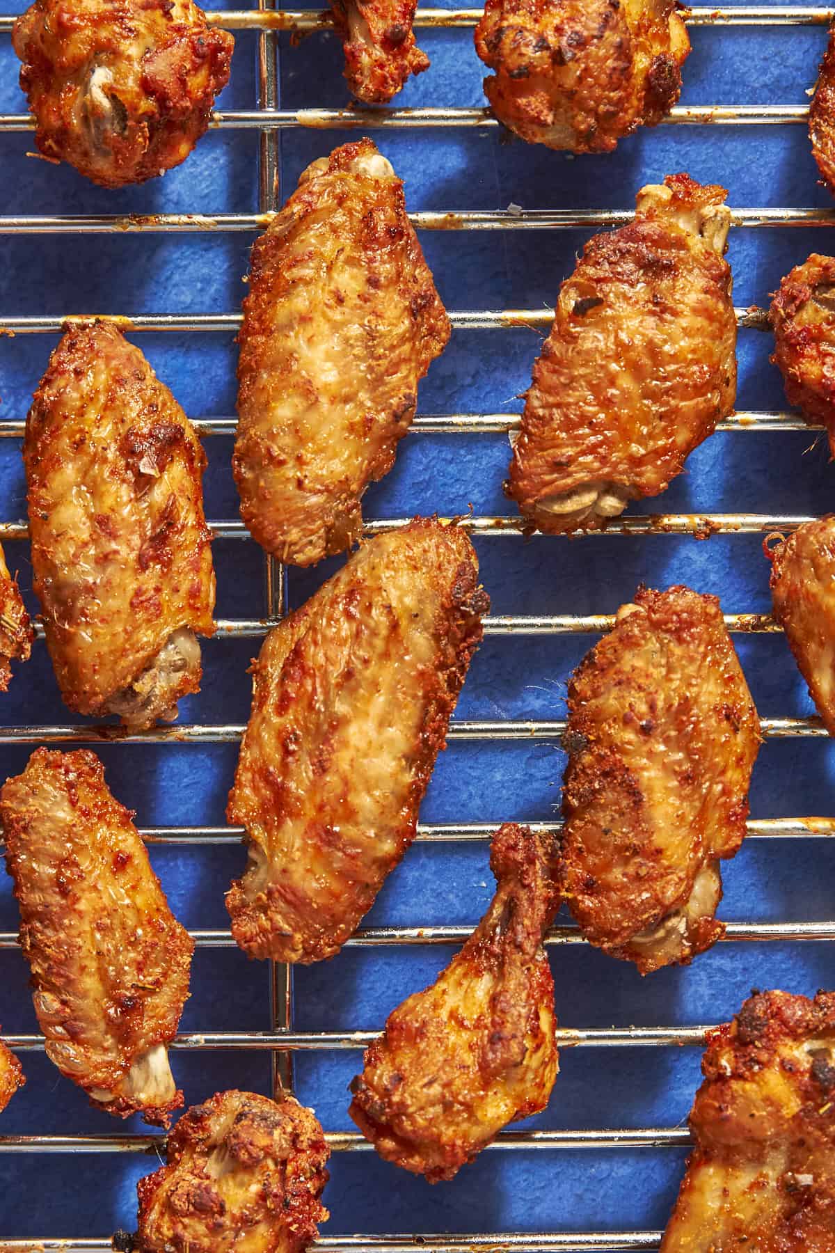 Golden brown, crispy chicken wings are arranged on a metal cooling rack over a bright blue background, highlighting the perfection you get when you know exactly how long to bake chicken wings at 400 degrees for the ideal texture.