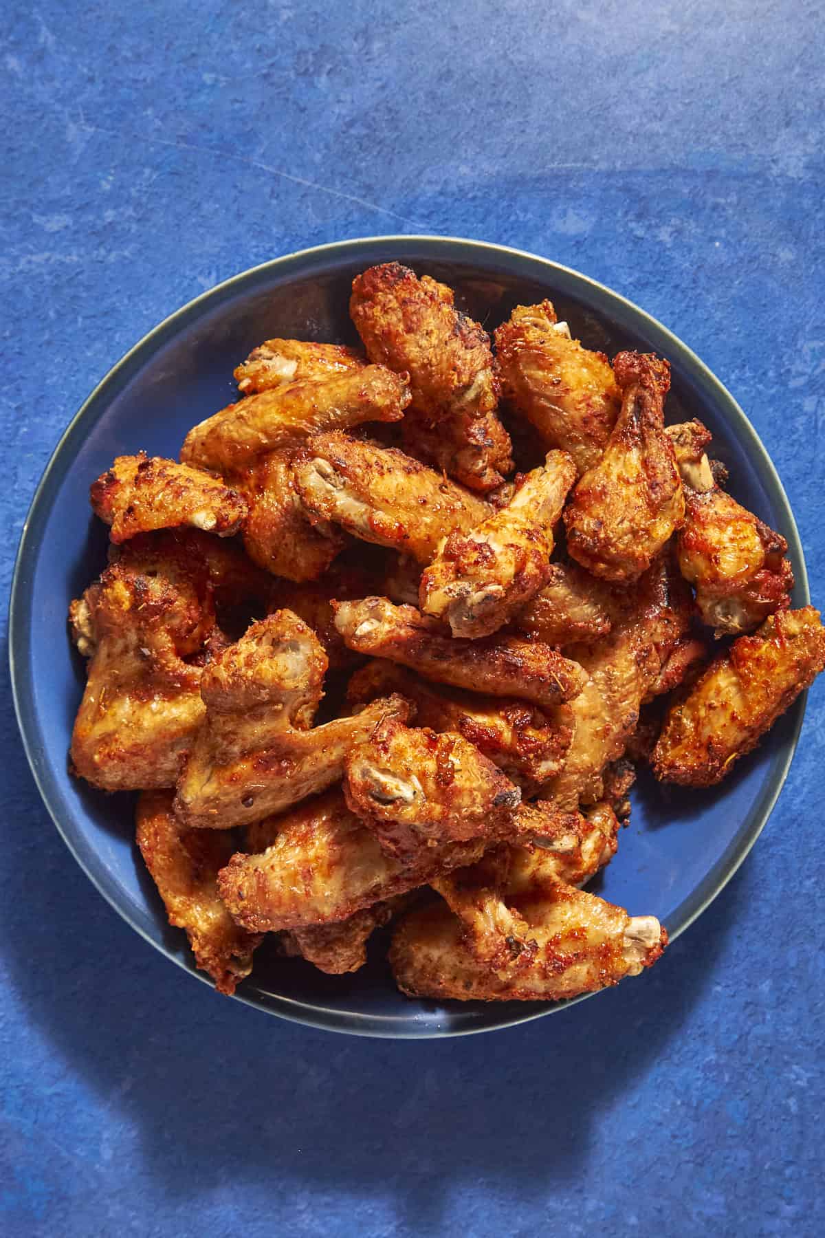 A large plate filled with crispy, golden-brown fried chicken wings, set on a bright blue tabletop—these could be yours if you know how long to bake chicken wings at 400 for perfect results every time.
