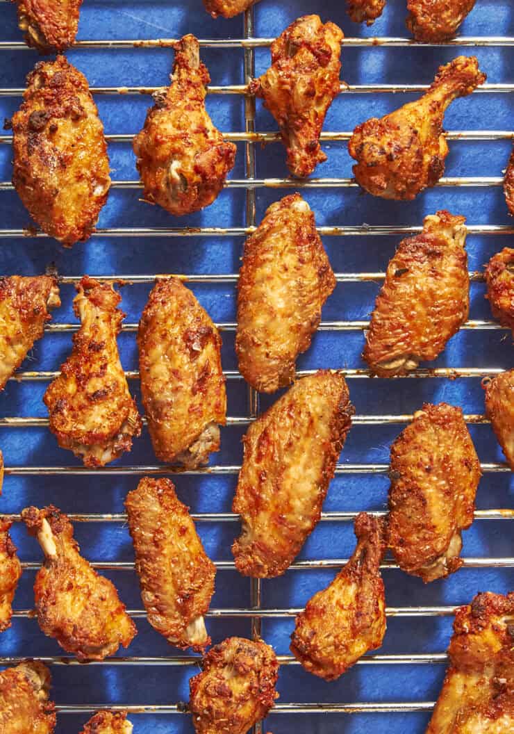 Rows of crispy, golden-brown chicken wings and drumettes are arranged on a metal wire rack above a vibrant blue background, their textured skin perfectly seasoned—just what you’d expect when following tips for how long to bake chicken wings at 400.
