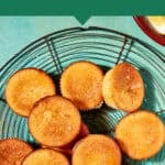 Overhead view of a cooling rack topped with golden lemon muffins arranged in a circle on a light blue background. Text above reads Lemon Drizzle Muffins—Ideal for a Crowd.