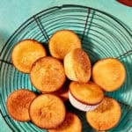 Overhead view of golden lemon muffins on a cooling rack, with fresh lemon wedges in a bowl, a cup of tea, and text reading The Best Lemon Muffins Recipe—Quick and Simple and www.beatthebudget.com.