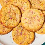 A plate of golden-brown Funfetti Cookies topped with colorful sprinkles sits on a light blue surface. Text at the bottom reads Funfetti Cookies and www.beatthebudget.com.