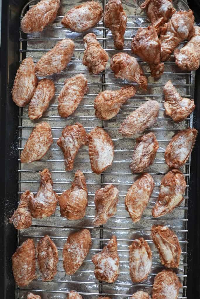 Raw chicken wings coated with seasoning are arranged in rows on a metal rack over a baking tray, ready to become delicious baked chicken wings.