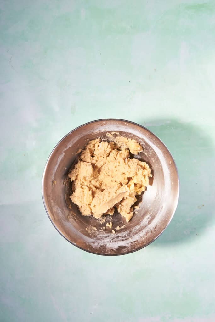 A metal mixing bowl containing a thick, beige dough sits on a light blue, textured surface.