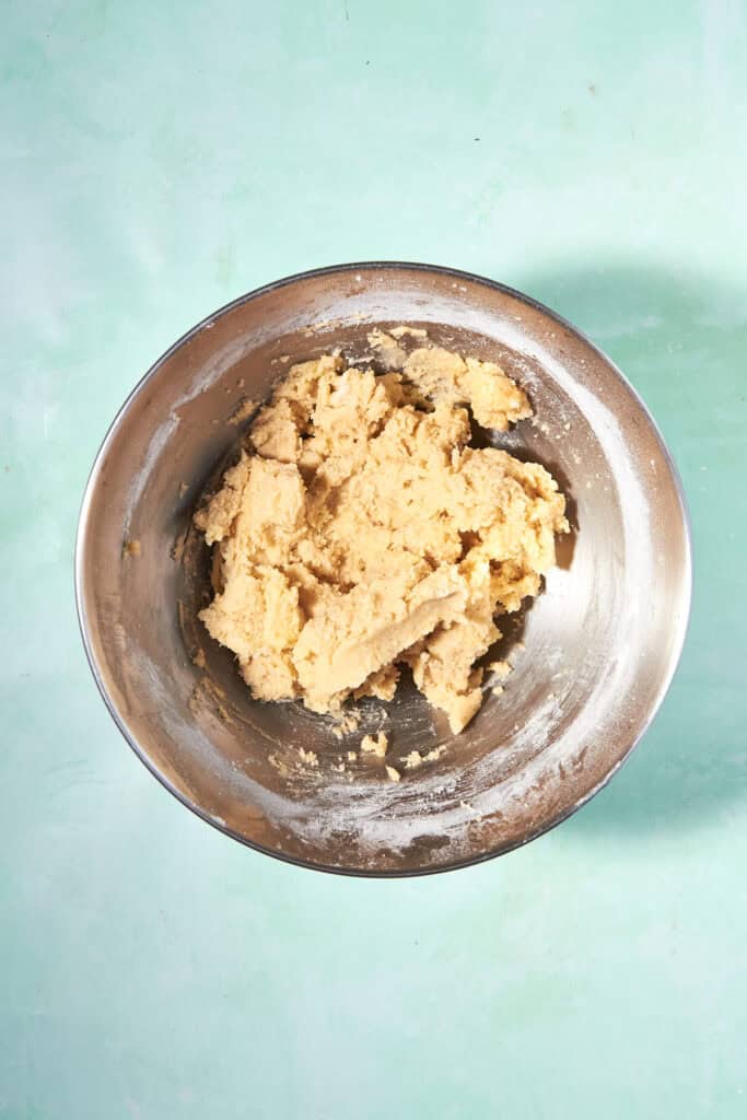 A metal mixing bowl filled with raw cookie dough sits on a light turquoise surface.