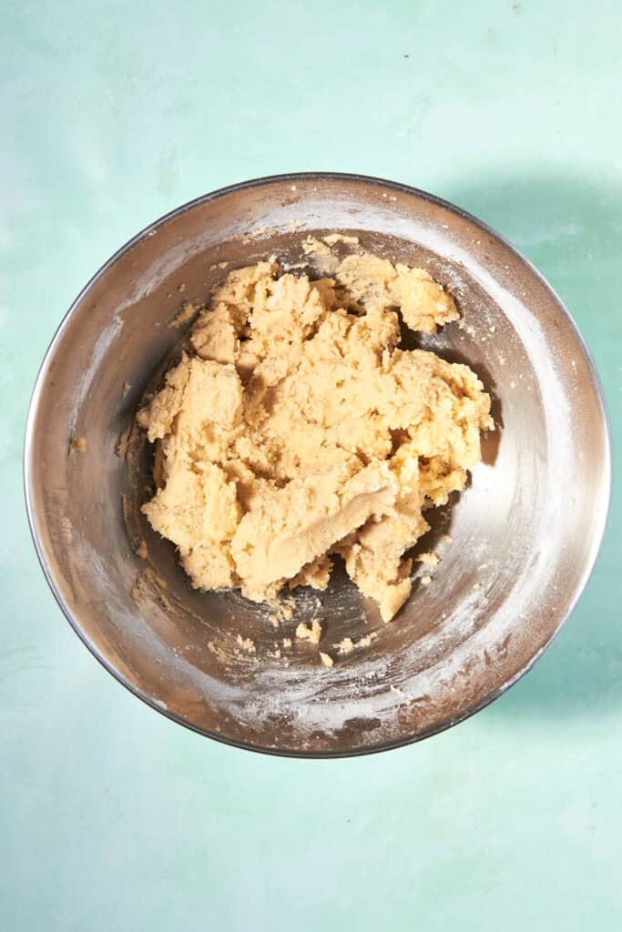 A metal mixing bowl filled with pale shortcake biscuit dough sits on a light blue, textured surface.