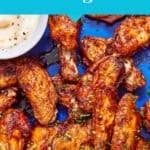 A tray of extra crispy baked chicken wings garnished with chopped herbs, served with a bowl of creamy dipping sauce. Text reads: No deep frying needed! Enjoy delicious, extra crispy baked chicken wings.