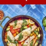 Top-down view of a skillet with cooked sea bass fillets, cherry tomatoes, green olives, zucchini, lemon slices, and green herb sauce on a blue surface. Text above reads: Easy Summer Sea Bass Recipe—your new favorite sea bass recipe.