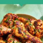 A bowl of baked chicken drumsticks garnished with chopped herbs sits on a green surface. The text reads Popular Recipe: Baked Chicken Leg Recipe with the website www.beatthebudget.com at the bottom.