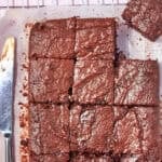 A batch of sweet potato brownies cut into squares on parchment paper, resting on a cooling rack. A butter knife lies beside the sweet potato brownies. Text reads Sweet Potato Brownies and www.beatthebudget.com.