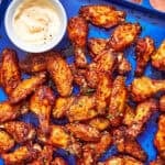 A blue tray filled with crispy baked chicken wings, garnished with herbs, and served with a small bowl of dipping sauce. Text on the image reads, Baked Chicken Wings and www.beatthebudget.com.