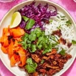 A bowl with rainbow noodles, shredded red cabbage, carrot ribbons, cilantro, spicy ground meat, a lime wedge, and chili flakes. Surrounding the bowl are similar salad bowls. Text reads: Rainbow Noodle Salad Bowls and www.beatthebudget.com.