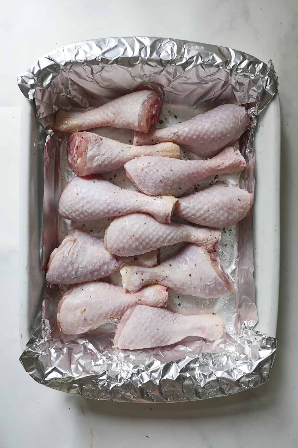 Butter-basted chicken drumsticks arranged skin-side up on a baking tray