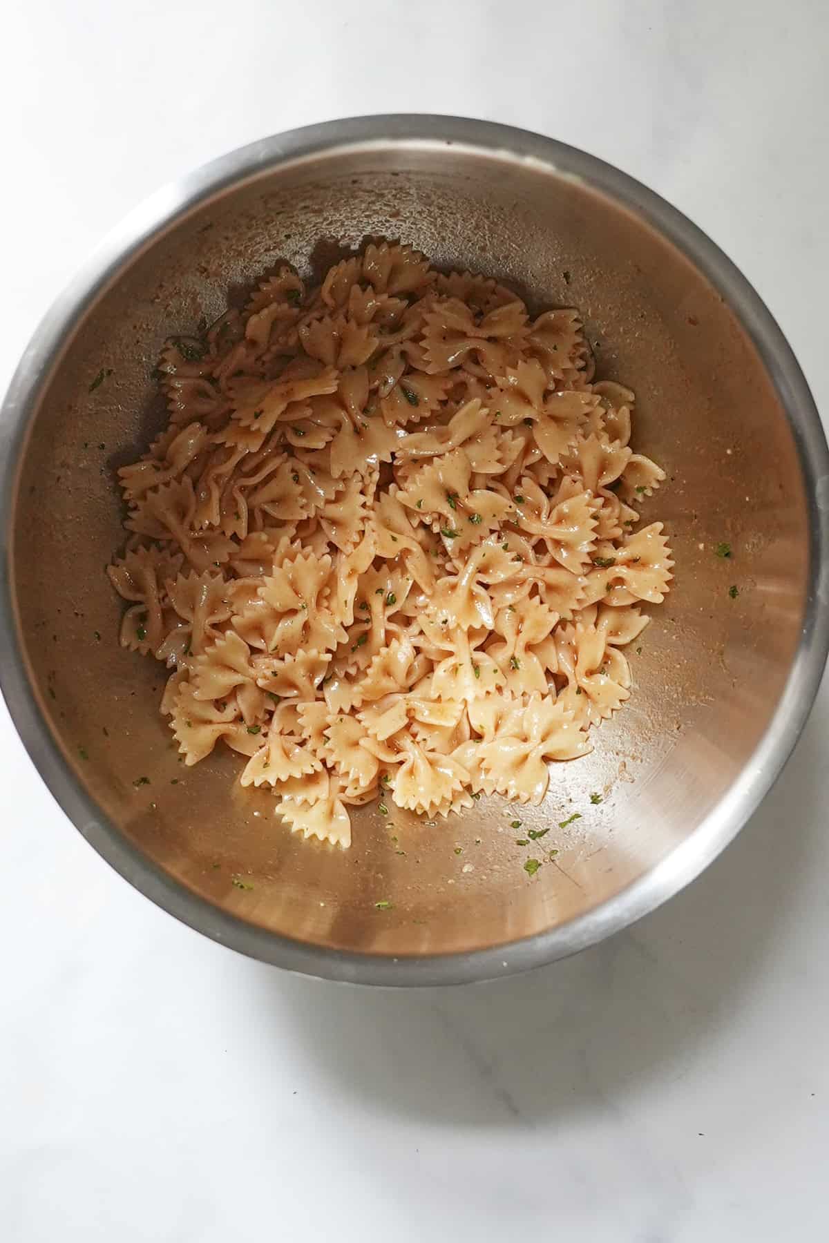 Cooked farfalle pasta tossed through the smoky paprika dressing in a large bowl
