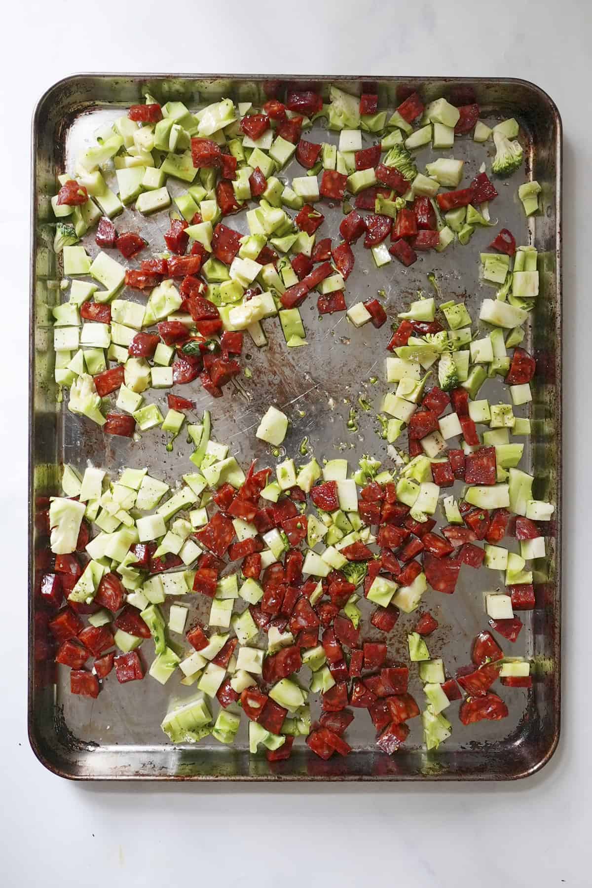 Broccoli stalks and chorizo chunks in a baking tray coated in olive oil
