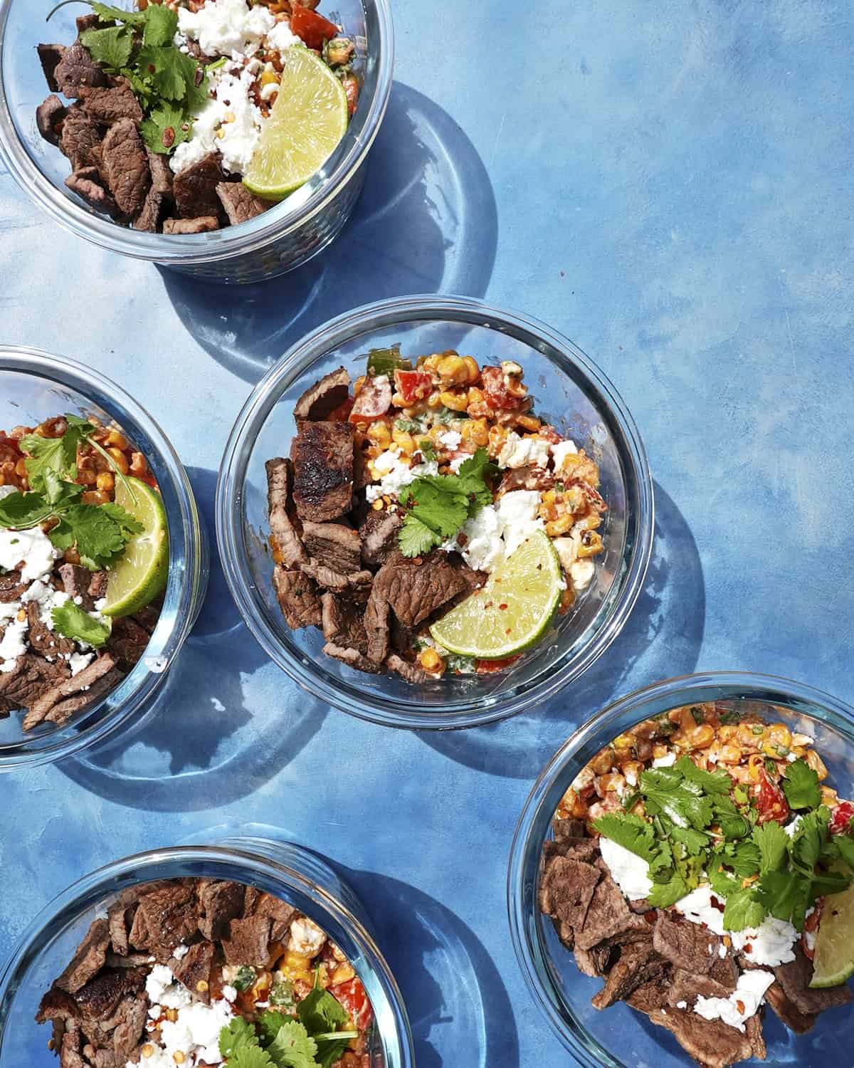 Cajun steak salad in meal prep containers with lime wedges and feta