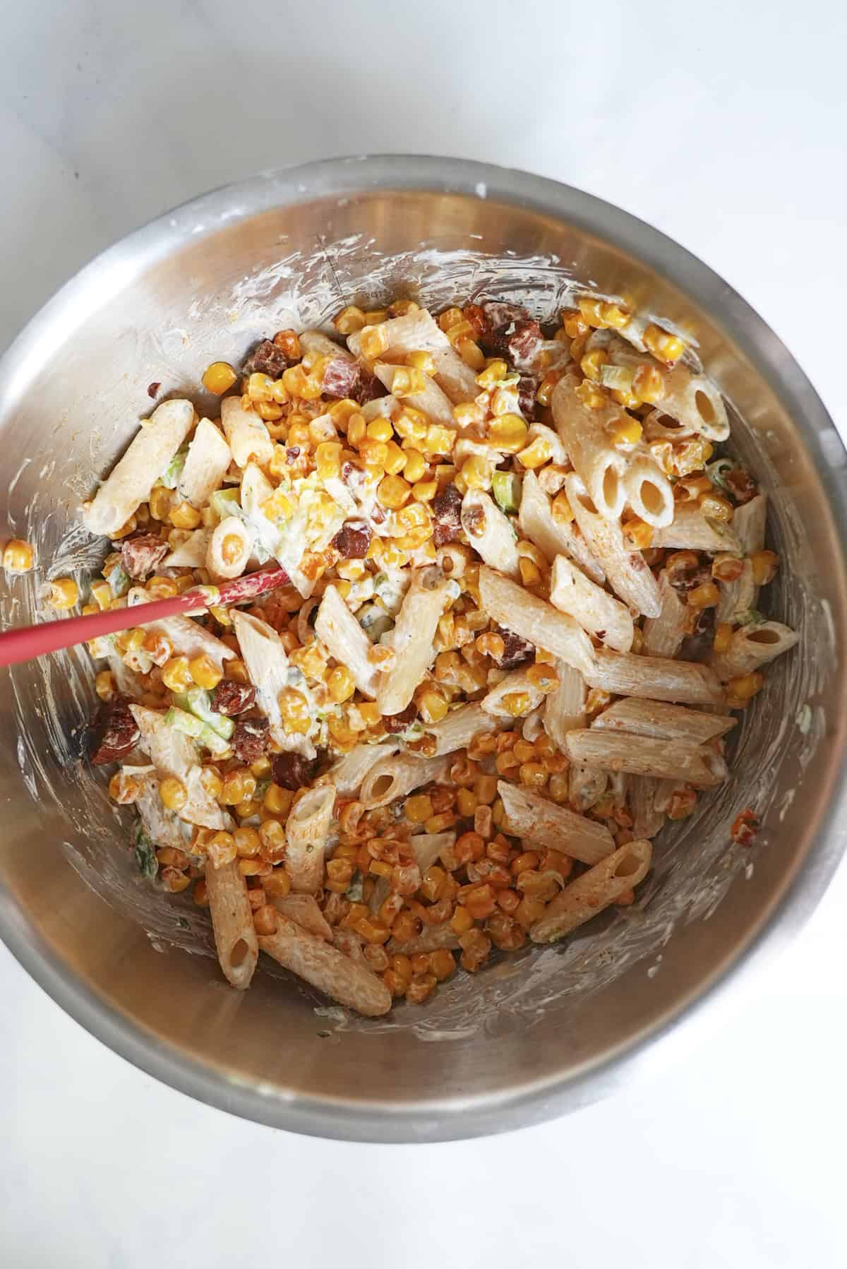 Pasta, tzatziki and spring onion being stirred together in a large bowl
